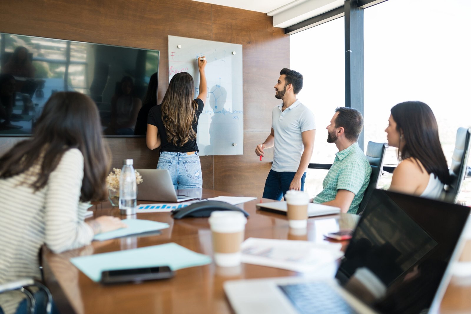 Colleagues looking at businesswoman writing on whiteboard at office during presentation